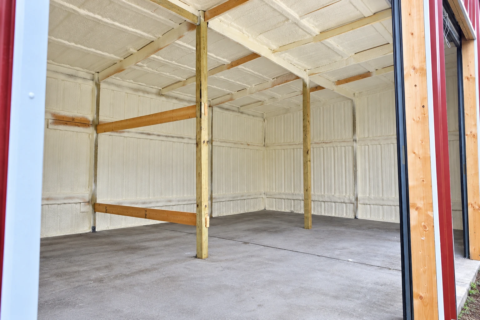 Empty commercial building interior with white spray foam insulation across the walls and ceiling, framed by wooden beams.