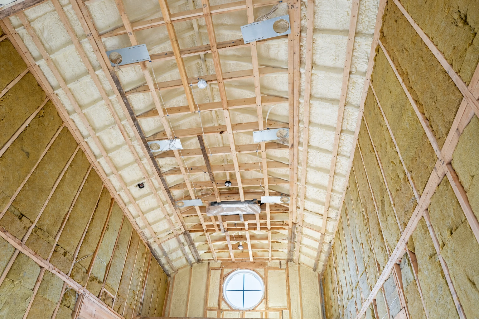 Spray foam insulation fills the roof and wall cavities of a timber-framed room with a round window.